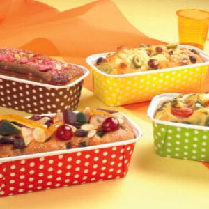 Colorful assortment of rectangular cakes in polka-dot baking cups on a bright party table, topped with fruits and nuts