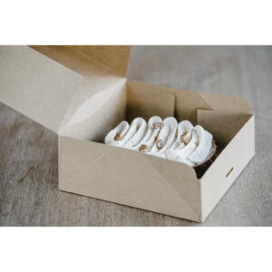Open brown cardboard box reveals a cake with white piped frosting on a wooden surface, ready to serve.